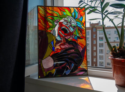 Creepy clown stained glass panel leaning on windowsill indoors, vibrant red orange green handmade Tiffany copper foil art
