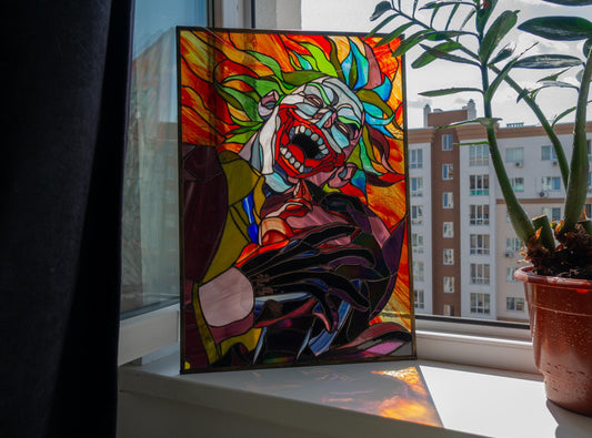 Creepy clown stained glass panel leaning on windowsill indoors, vibrant red orange green handmade Tiffany copper foil art