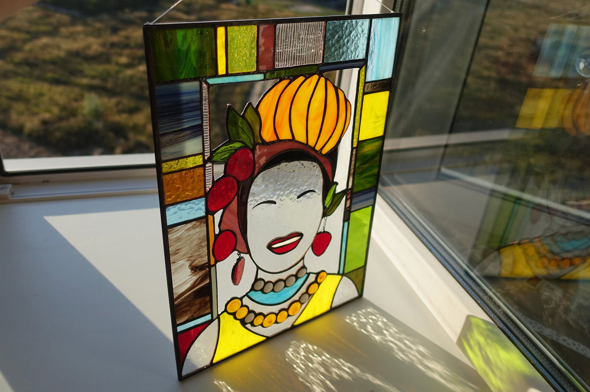 Stained glass panel of a woman's face with colorful frame on a reflective surface