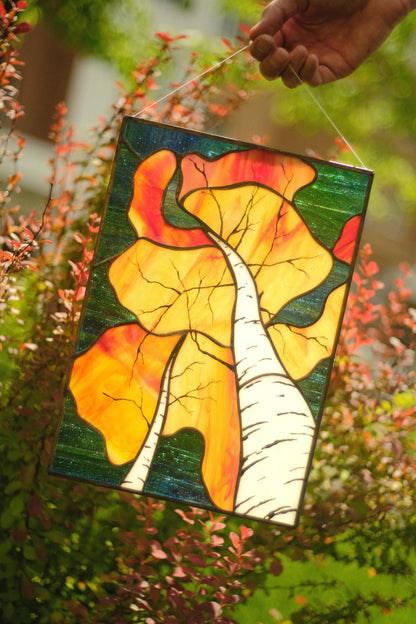 Stained glass panel with autumn leaves held in front of a natural background