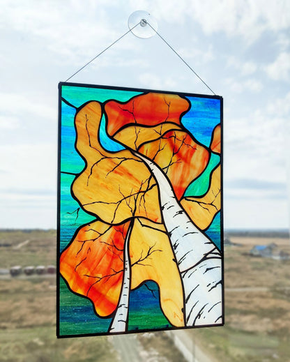 Stained glass panel with autumn leaves and a birch tree against a blue sky.