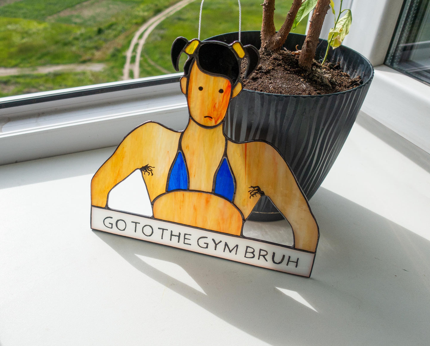 Handmade glass bodybuilder suncatcher hanging in window — funny fitness gift, colorful light catcher