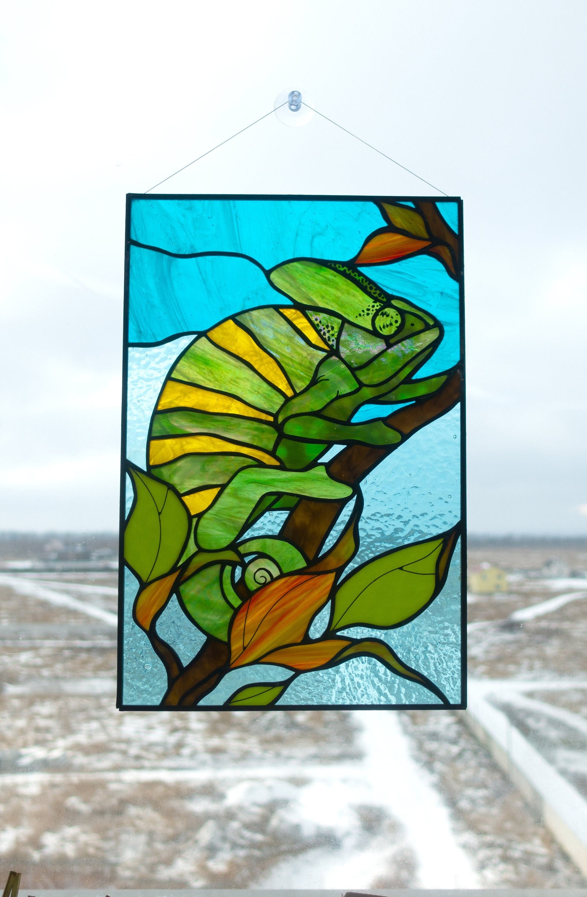 Stained glass chameleon close-up — curling tail on branch, black patina finish, hand-cut glass scales