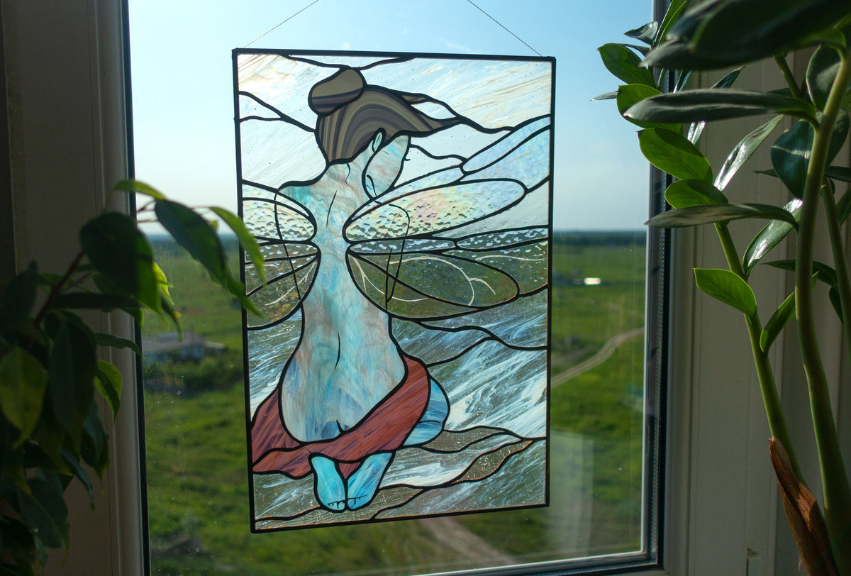  Stained glass fairy girl panel hanging in window between two plants, iridescent clear wings with teal body and burgundy skirt, blue sky background
