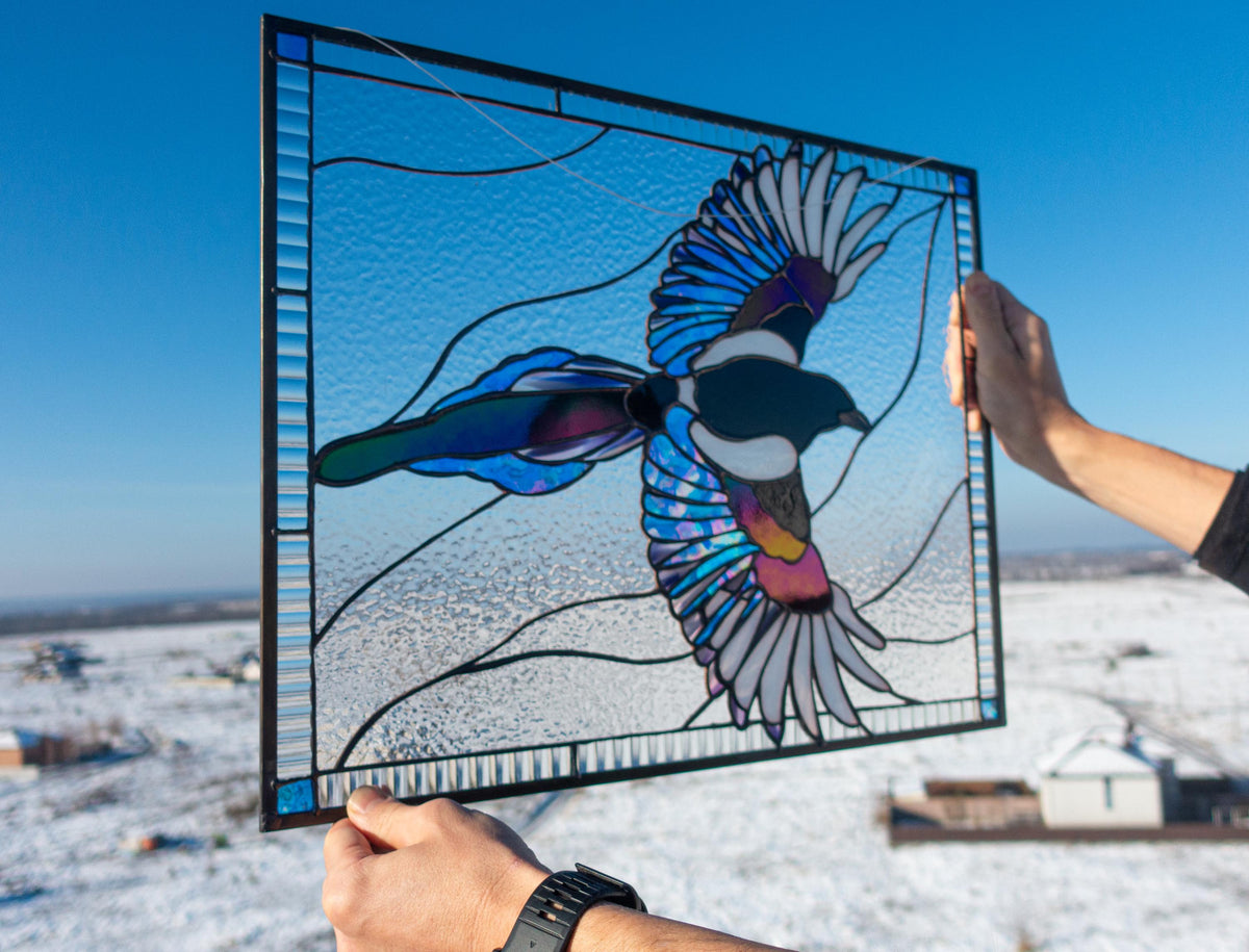 Stained glass magpie panel with lime green border hanging outdoors at sunset, iridescent green and blue wings, handmade bird window art
