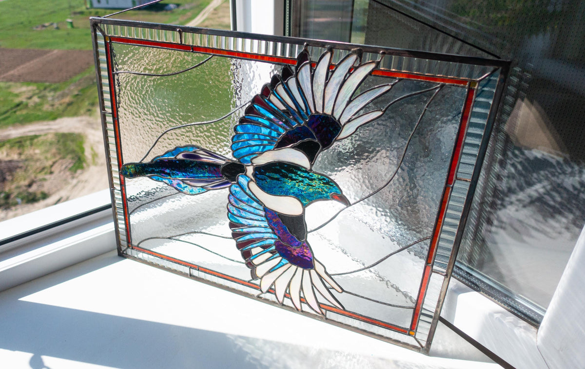 Large stained glass flying magpie panel held outdoors in winter light, iridescent blue purple wings, clear textured glass background