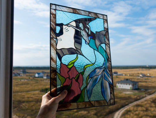 Handmade stained glass mermaid and stingray panel held up against blue sky, mermaid with teal tail swimming alongside white manta ray, copper foil technique