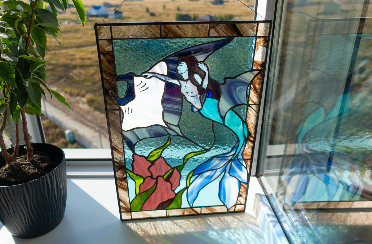 Stained glass mermaid and manta ray panel on windowsill with plant in sunlight, teal and blue ocean glass with red coral and green seaweed, Tiffany copper foil