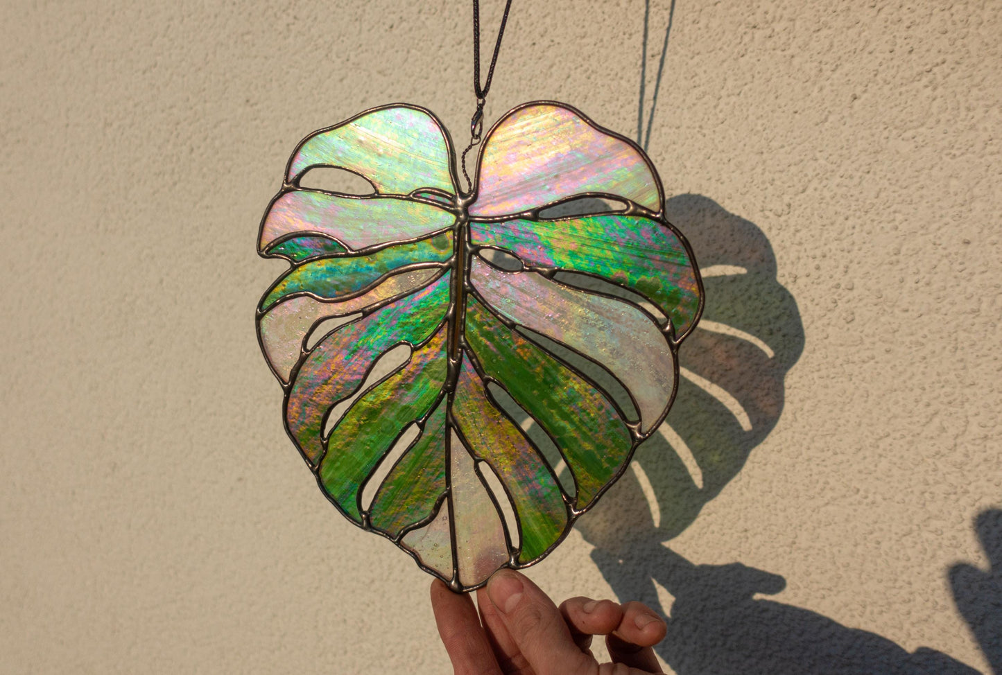 Iridescent monstera leaf stained glass close-up — split leaf fenestration detail, black patina finish