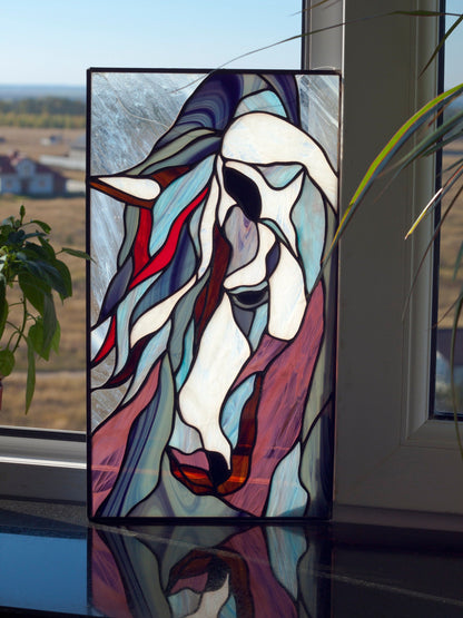 Stained glass mustang horse panel leaning against a window sill with countryside view, white horse face with flowing blue and red mane