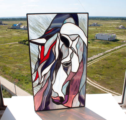 Handmade stained glass horse panel held up outdoors with aerial countryside background, abstract mustang portrait in blue, pink and red glass