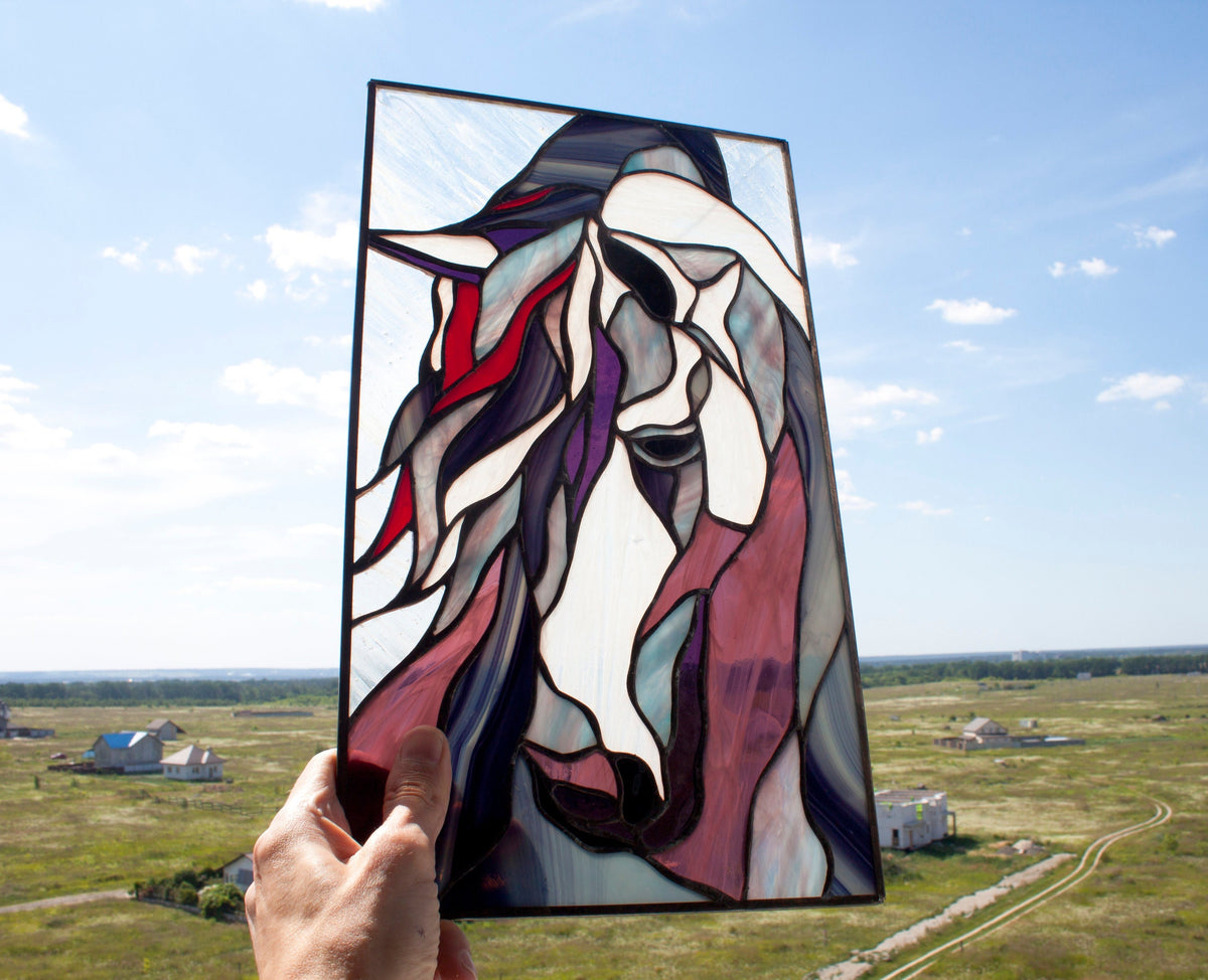 Stained glass mustang horse panel held up against blue sky, abstract horse head with flowing purple and red mane, copper foil technique