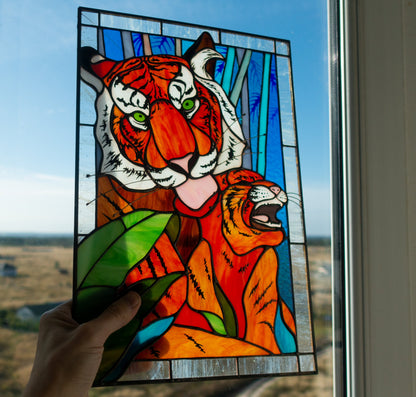 Stained glass panel of a tiger held against a window with a view of a field and blue sky.