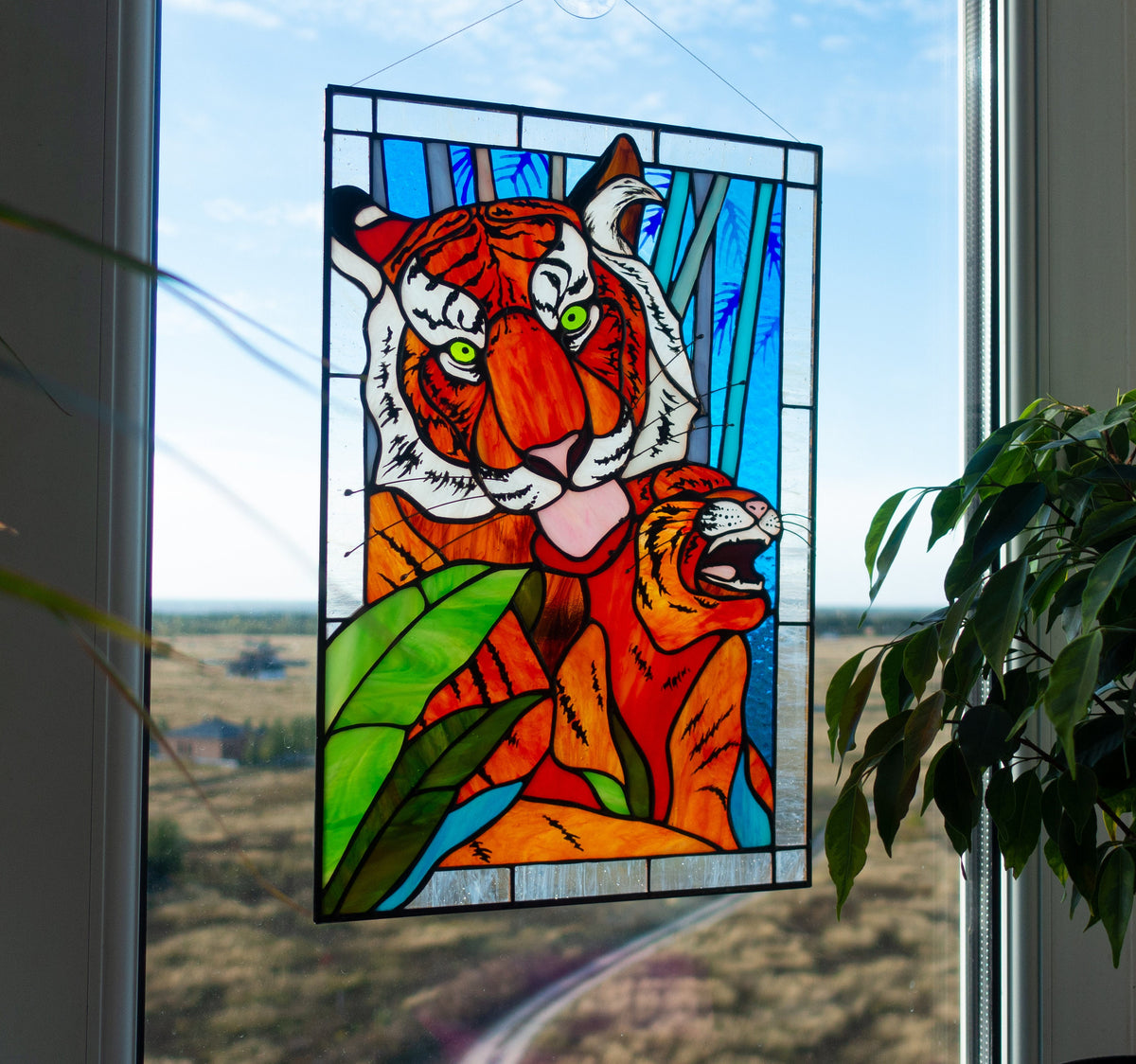 Stained glass panel of a tiger on a window with a view of a field.